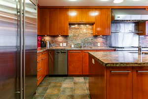 Kitchen featuring stone countertops, backsplash, stainless steel appliances, and sink