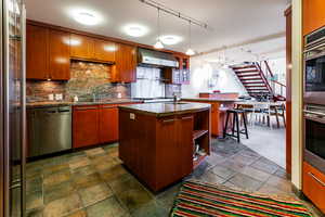 Kitchen featuring wall chimney exhaust hood, tasteful backsplash, a breakfast bar, a center island with sink, and appliances with stainless steel finishes