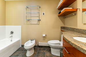 Bathroom with vanity, a bathtub, a bidet, toilet, and a baseboard radiator