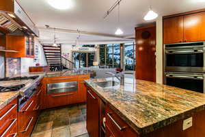 Kitchen featuring light stone countertops, a center island with sink, exhaust hood, and appliances with stainless steel finishes