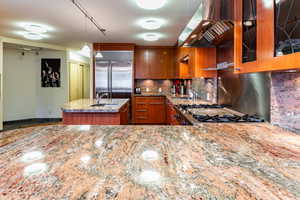 Kitchen featuring pendant lighting, a kitchen island with sink, sink, appliances with stainless steel finishes, and range hood