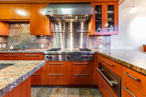 Kitchen featuring hanging light fixtures, tasteful backsplash, light stone counters, and stainless steel gas stovetop