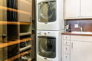 Clothes washing area with stacked washer / drying machine, cabinets, and sink