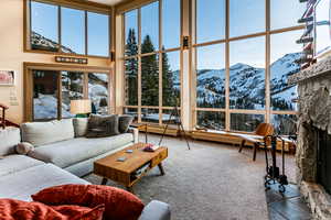 Carpeted living room with a mountain view, a stone fireplace, plenty of natural light, and a towering ceiling