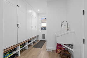 Mudroom with light hardwood / wood-style floors and sink. as well as a Roomba docking station.