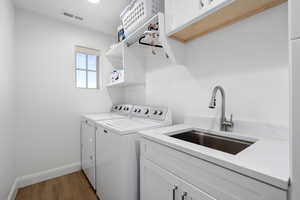 Clothes washing area with hardwood / wood-style flooring, cabinets, independent washer and dryer, and sink