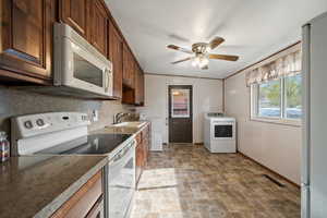 Kitchen with ceiling fan, sink, washer / dryer, vaulted ceiling, and white appliances