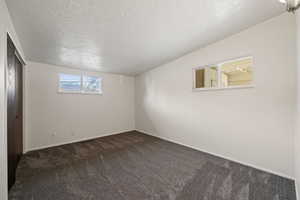 Carpeted empty room with a textured ceiling and vaulted ceiling