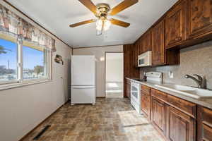 Kitchen with backsplash, dark brown cabinets, white appliances, ceiling fan, and sink