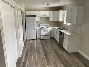 Kitchen featuring white appliances, dark wood-type flooring, sink, white cabinets, and hanging light fixtures