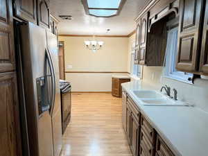 Kitchen with sink, hanging light fixtures, stainless steel appliances, light hardwood / wood-style flooring, and ornamental molding