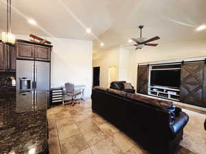 Living room with ceiling fan, a barn door, lofted ceiling, and light tile patterned floors