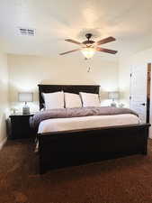 Bedroom with dark colored carpet, ceiling fan, and a textured ceiling