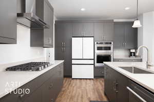 Kitchen with sink, light hardwood / wood-style flooring, wall chimney exhaust hood, appliances with stainless steel finishes, and decorative light fixtures