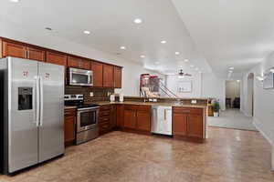 Kitchen with kitchen peninsula, appliances with stainless steel finishes, light stone countertops, backsplash, and ceiling fan