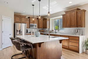 Kitchen with an island with sink, pendant lighting, a breakfast bar area, appliances with stainless steel finishes, and light wood-type flooring