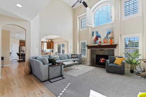 Living room with ceiling fan with notable chandelier, light hardwood / wood-style floors, high vaulted ceiling, and a tiled fireplace