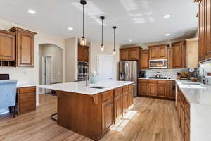 Kitchen with light wood-type flooring, stainless steel appliances, a center island with sink, and sink