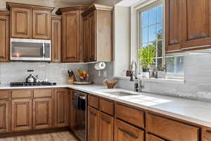 Kitchen featuring decorative backsplash, sink, stainless steel appliances, and light hardwood / wood-style flooring