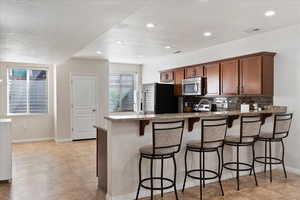 Kitchen featuring light stone countertops, backsplash, kitchen peninsula, a breakfast bar area, and appliances with stainless steel finishes