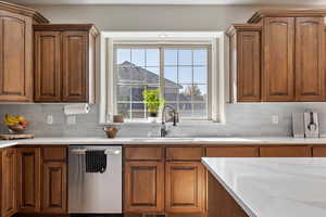 Kitchen with decorative backsplash, light stone counters, stainless steel dishwasher, and sink