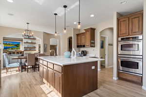 Kitchen with a chandelier, stainless steel double oven, pendant lighting, and light hardwood / wood-style floors