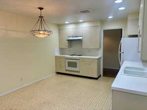 Kitchen with sink, white appliances, hanging light fixtures, and exhaust hood