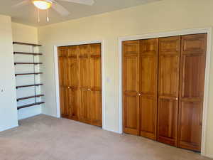 Unfurnished bedroom featuring ceiling fan, light colored carpet, and multiple closets