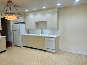 Kitchen featuring white cabinets, pendant lighting, white appliances, and sink