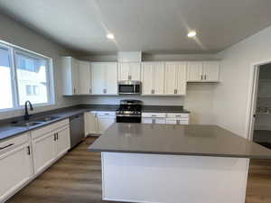 Kitchen featuring a center island, dark wood-type flooring, white cabinets, sink, and appliances with stainless steel finishes