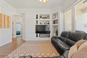 Living room with crown molding, built in features, and light wood-type flooring