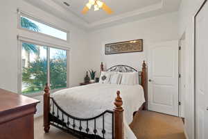 Bedroom featuring a raised ceiling, ceiling fan, and carpet flooring