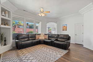 Living room with ceiling fan, built in features, wood-type flooring, and crown molding