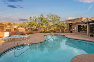 Pool at dusk with an in ground hot tub and a patio