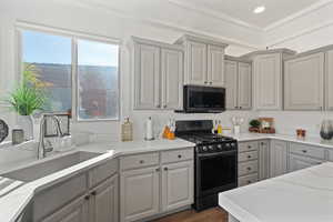 Kitchen with light stone countertops, dark hardwood / wood-style flooring, gray cabinetry, sink, and black gas range