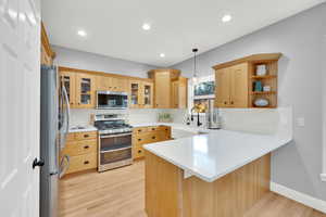 Kitchen featuring kitchen peninsula, appliances with stainless steel finishes, light wood-type flooring, hanging light fixtures, and a breakfast bar area