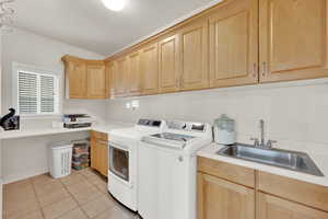 Laundry room featuring cabinets, light tile patterned floors, sink, and washing machine and clothes dryer