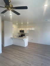 Kitchen with appliances with stainless steel finishes, light wood-type flooring, a kitchen breakfast bar, ceiling fan, and white cabinets