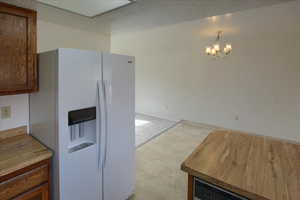 Kitchen with pendant lighting, white fridge with ice dispenser, a textured ceiling, and an inviting chandelier