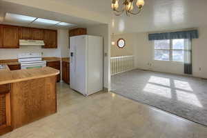 Kitchen featuring pendant lighting, white appliances, light carpet, kitchen peninsula, and a chandelier