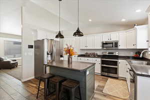 Kitchen with sink, light hardwood / wood-style flooring, vaulted ceiling, appliances with stainless steel finishes, and white cabinetry