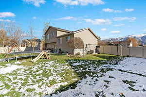 Snow covered property featuring a mountain view, a yard, and a trampoline