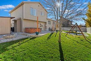 Rear view of property featuring a lawn, a playground, a patio, and a hot tub