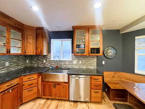 Cherry Wood Kitchen with sink, tasteful backsplash, stainless steel dishwasher, dark stone counters, and light hardwood flooring