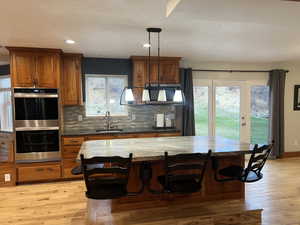 Kitchen with sink, light hardwood flooring, double oven, decorative light fixtures, and a breakfast bar