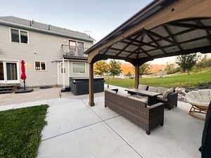 Patio terrace at dusk with a gazebo, a balcony off the house, an outdoor living space, a hot tub, and a lawn