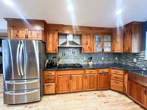 Cherry Wood Kitchen with decorative backsplash, hardwood flooring, stainless steel refrigerator, and wall chimney exhaust hood