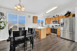 Kitchen featuring a breakfast bar, stainless steel appliances, vaulted ceiling, dark wood-type flooring, and decorative light fixtures