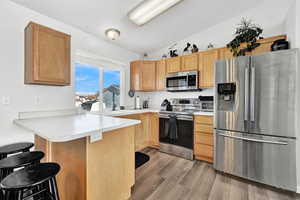 Kitchen with a kitchen bar, appliances with stainless steel finishes, light wood-type flooring, kitchen peninsula, and lofted ceiling