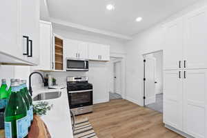 Kitchen with stainless steel appliances, light hardwood / wood-style flooring, white cabinetry, and sink